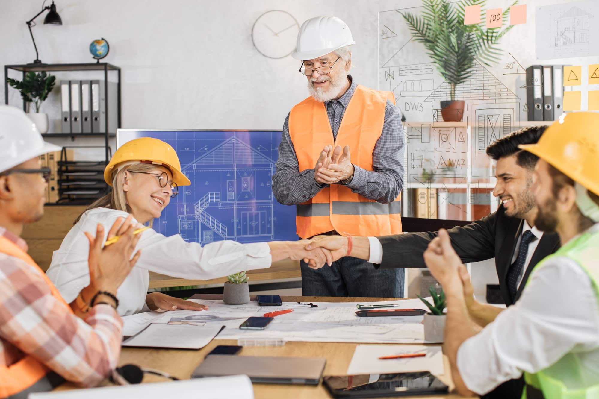 Happy construction team shaking hands during conference at office.